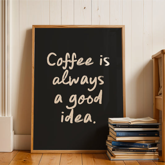 A framed poster with the text "Coffee is always a good idea" is displayed on a wooden floor next to a stack of books.