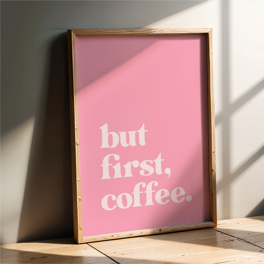 A framed poster with the text "but first, coffee" in white letters against a pink background.