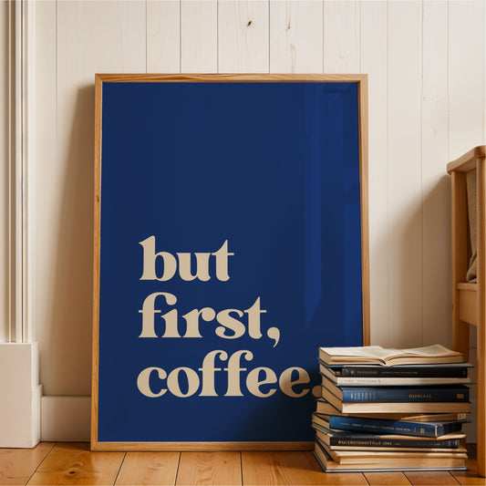 A blue poster with the text "but first, coffee" is leaning against a wall, with a stack of books next to it.