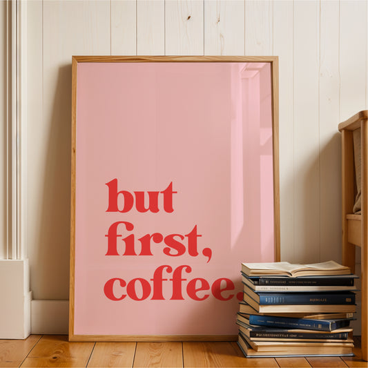 A framed poster with the text "but first, coffee" is leaning against a wall, with a stack of books next to it.