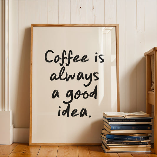 A framed poster with the text "Coffee is always a good idea" is displayed on a wooden floor next to a stack of books.