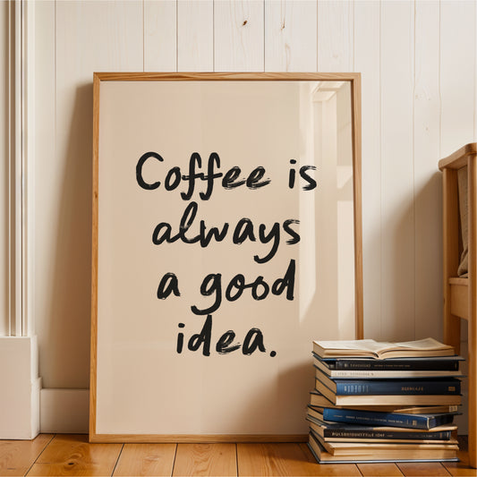A framed poster with the text "Coffee is always a good idea" is displayed on a wooden floor next to a stack of books.