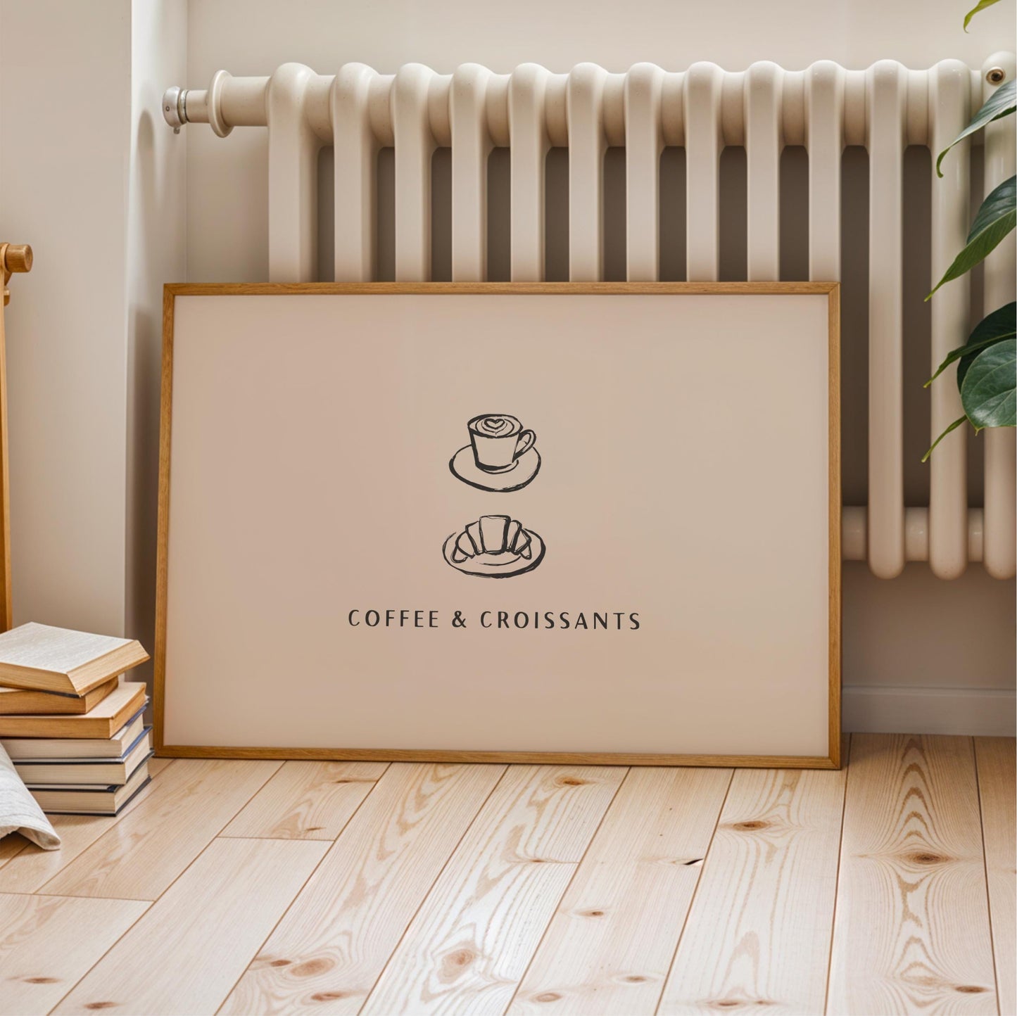 A framed poster with the text "COFFEE & CROISSANTS" and two illustrations of a coffee cup and a croissant, placed on a wooden floor next to a radiator.
