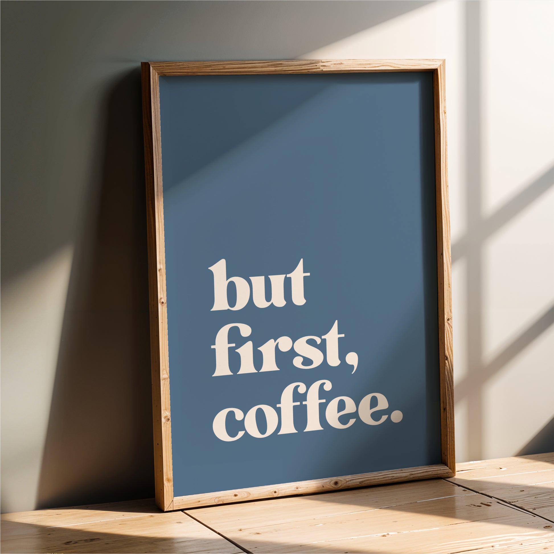 A framed poster with the text "but first, coffee" on it, leaning against a wall.