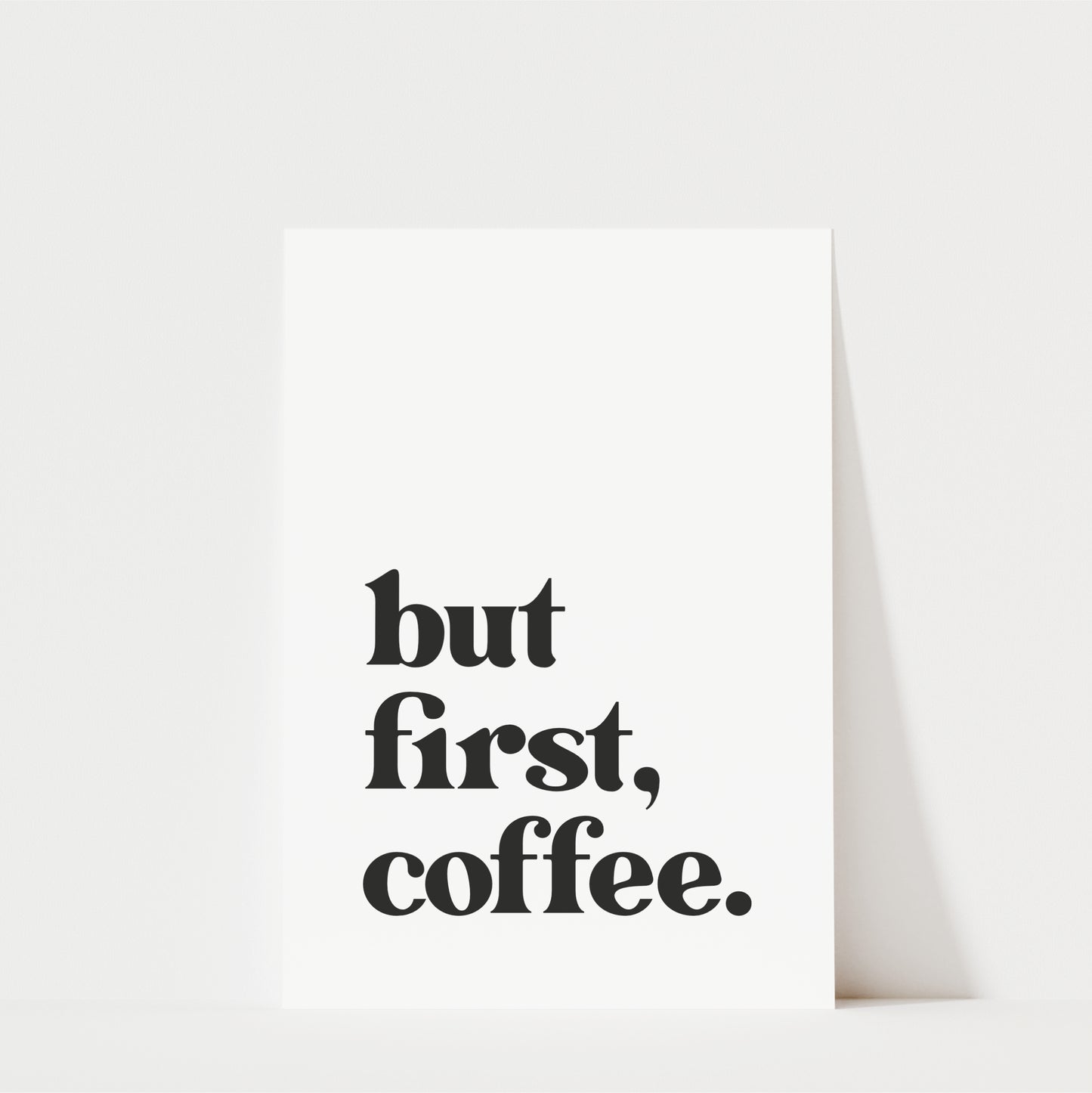 A white poster with the text "but first, coffee." printed on it.