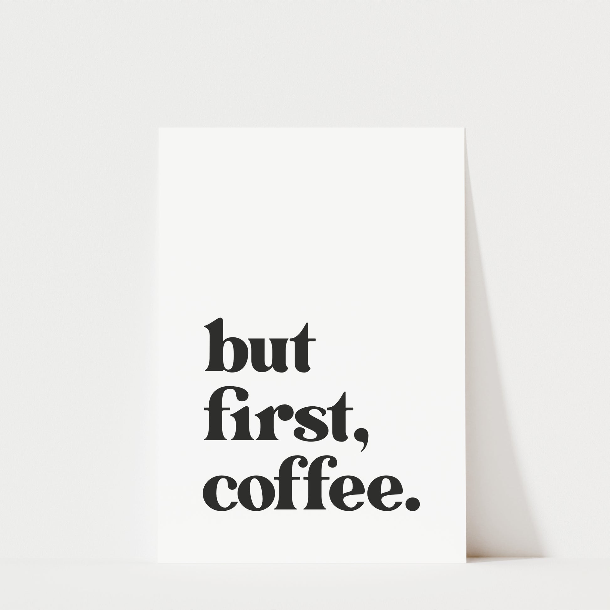 A white poster with the text "but first, coffee." printed on it.