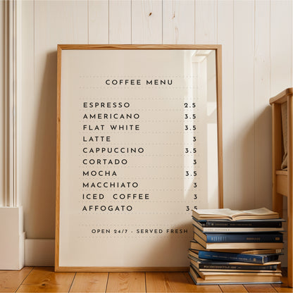 A framed coffee menu is displayed on a wooden floor next to a stack of books.