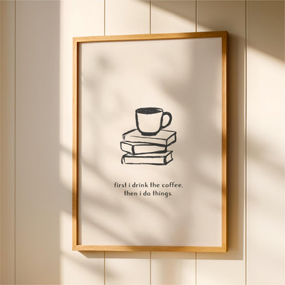 A framed poster with a simple black and white illustration of a cup of coffee on top of a stack of books, accompanied by the text "first I drink the coffee. Then I do things."