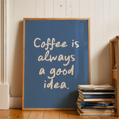 A framed poster with the text "Coffee is always a good idea" is displayed on a wooden floor next to a stack of books.