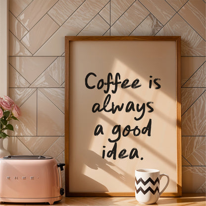 a framed quote that reads "Coffee is always a good idea." The quote is written in a casual, handwritten style. The frame is placed next to a pink toaster, and there is a white mug with a zigzag pattern on it. The background has a tiled wall, and there is a vase with pink roses on the counter.