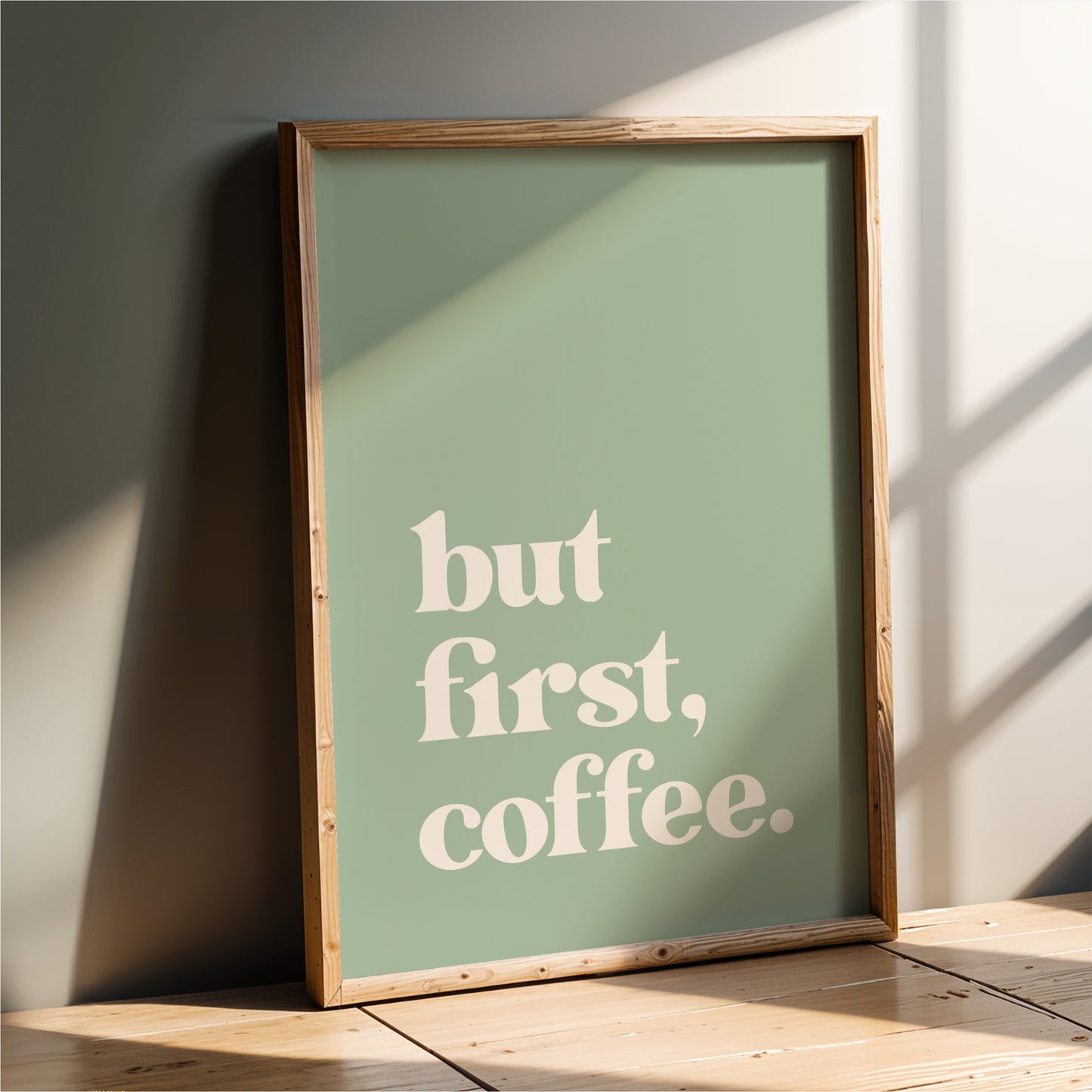 A framed poster with the text "but first, coffee" on it, leaning against a wall.
