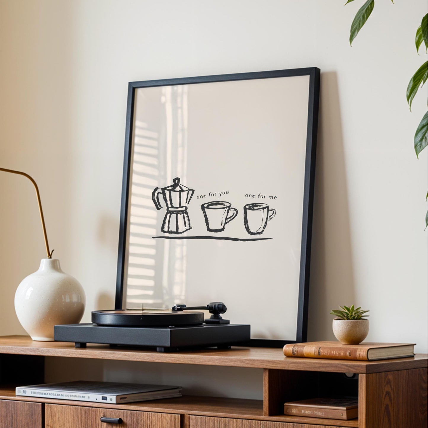 a framed poster with a simple black and white illustration of a coffee pot and two cups, accompanied by the text "one for you one for me". The poster is displayed on a wooden shelf, which also holds a record player and some books.
