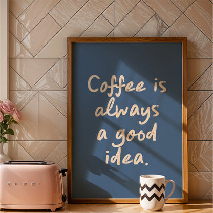 a framed poster with the text "Coffee is always a good idea" in a blue background, placed on a kitchen counter next to a pink toaster and a white coffee mug.
