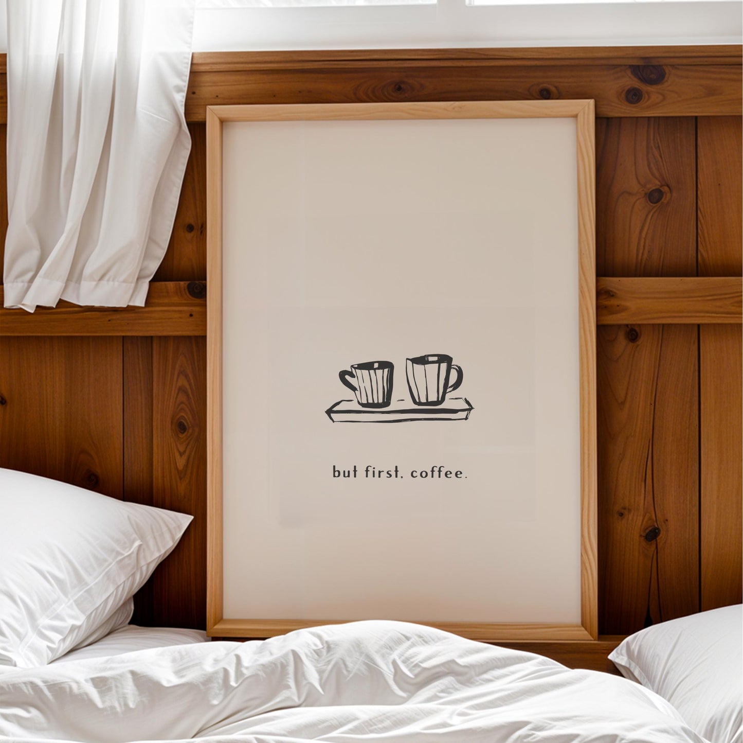a framed poster with a simple black and white illustration of two coffee cups on a tray, accompanied by the text "but first. coffee."