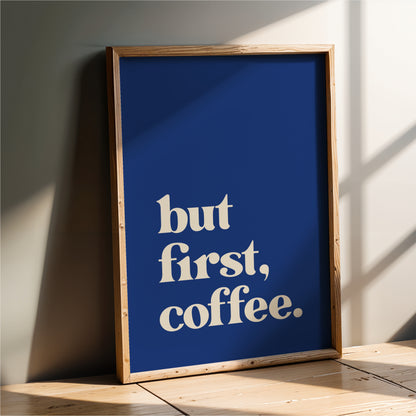 A framed poster with the text "but first, coffee" in white letters against a blue background.