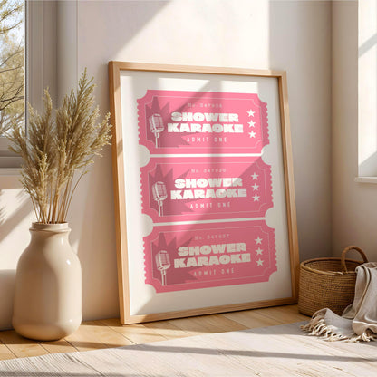 A framed poster advertising karaoke events, with three pink tickets featuring a microphone and the text "SHOWER KARAOKE" and "RUMIT ONE" printed on it. The poster is displayed on a wooden floor next to a vase with dried plants, and a woven basket is visible in the background.