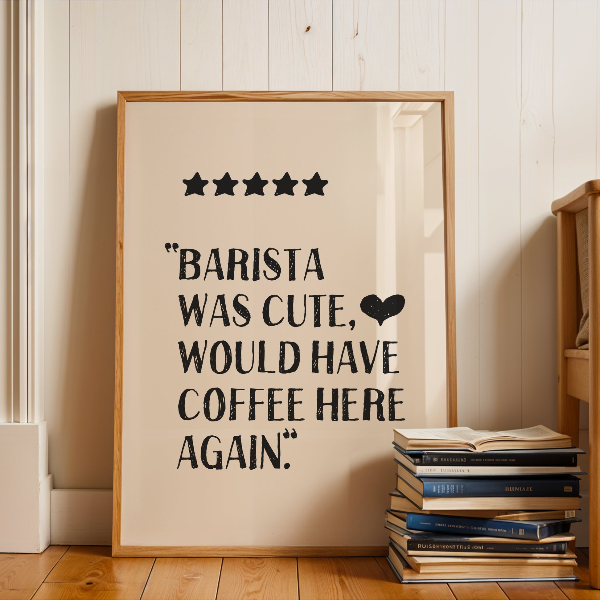 a framed poster with a text that reads "BARISTA WAS CUTE, WOULD HAVE COFFEE HERE AGAIN." The poster is placed on a wooden floor next to a stack of books.