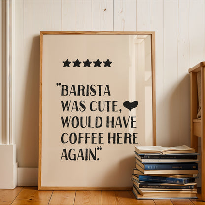 a framed poster with a text that reads "BARISTA WAS CUTE, WOULD HAVE COFFEE HERE AGAIN." The poster is placed on a wooden floor next to a stack of books.
