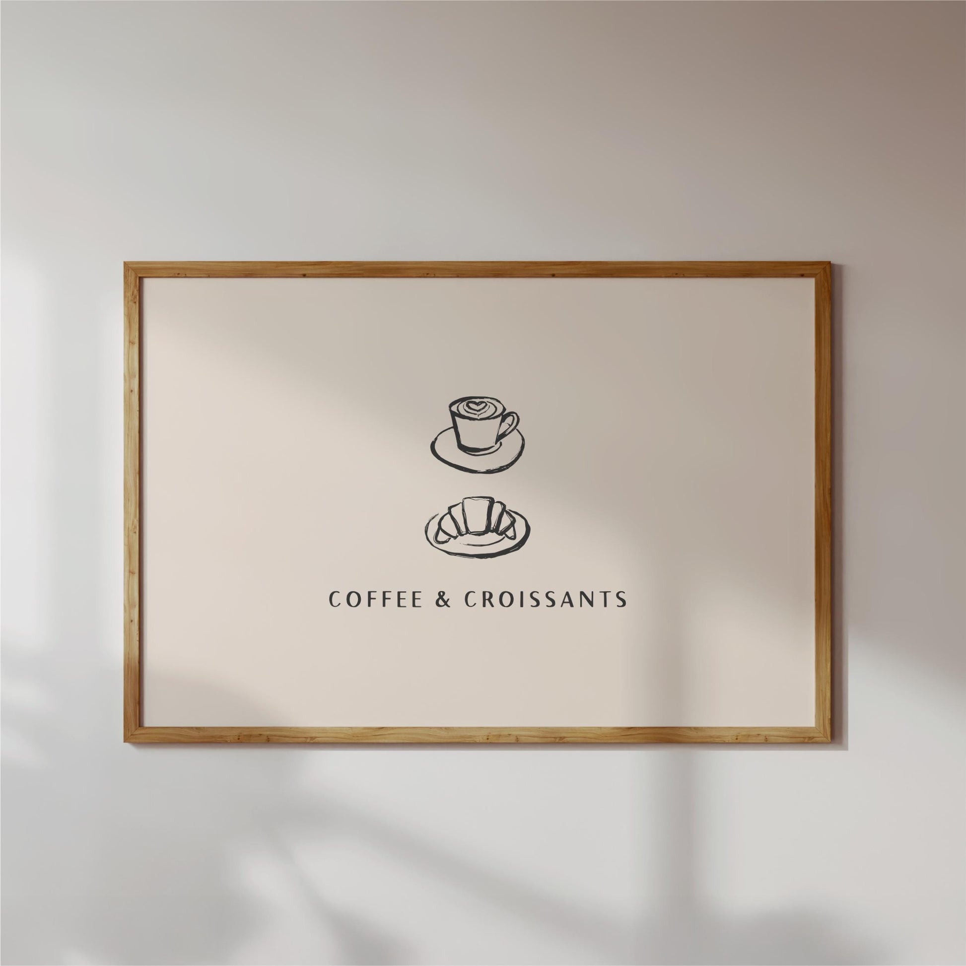 a framed poster with a simple illustration of a coffee cup and croissant, accompanied by the text "COFFEE & CROISSAINS" in a black font.