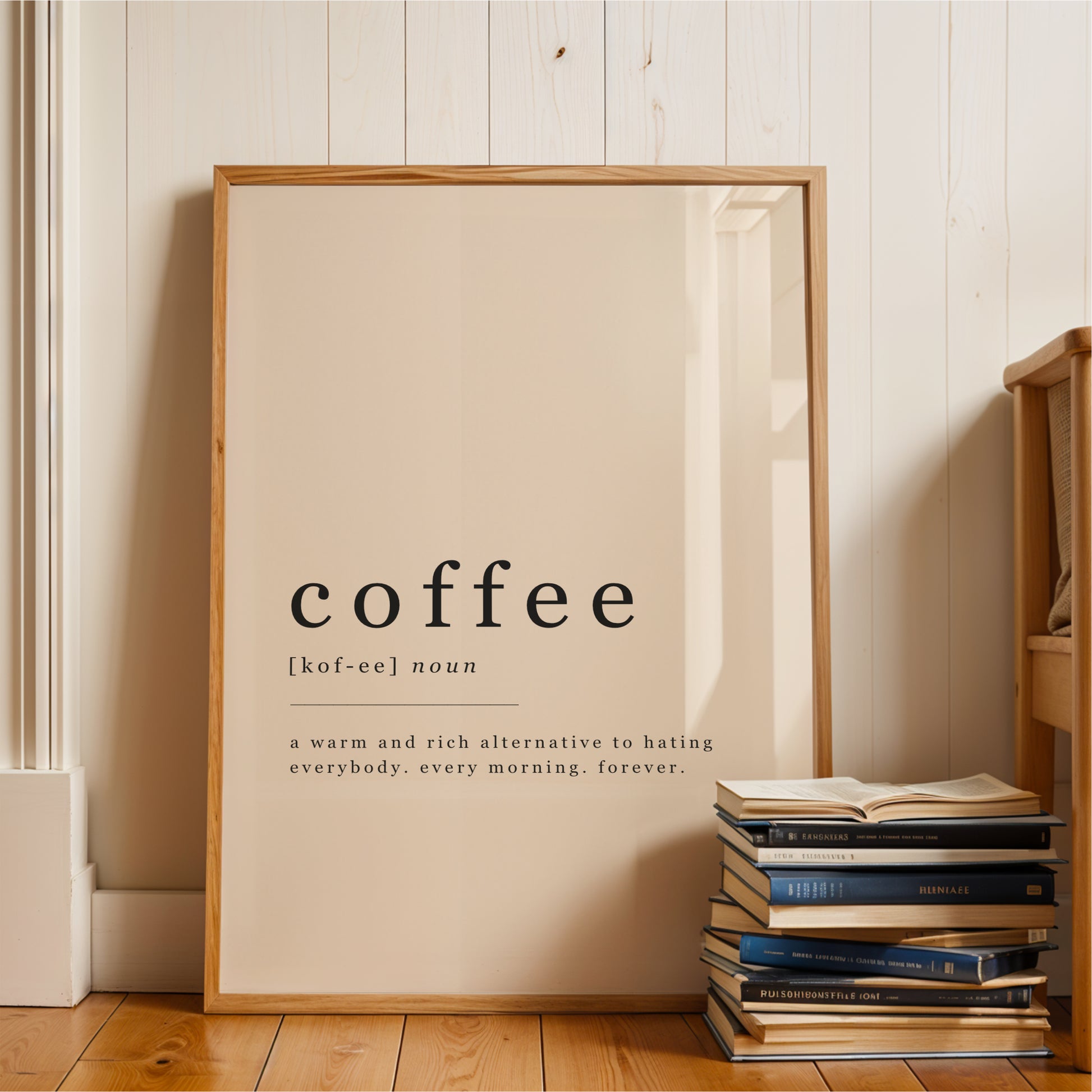 A wooden frame with a definition of coffee in bold black text, standing next to a stack of books on a wooden floor.