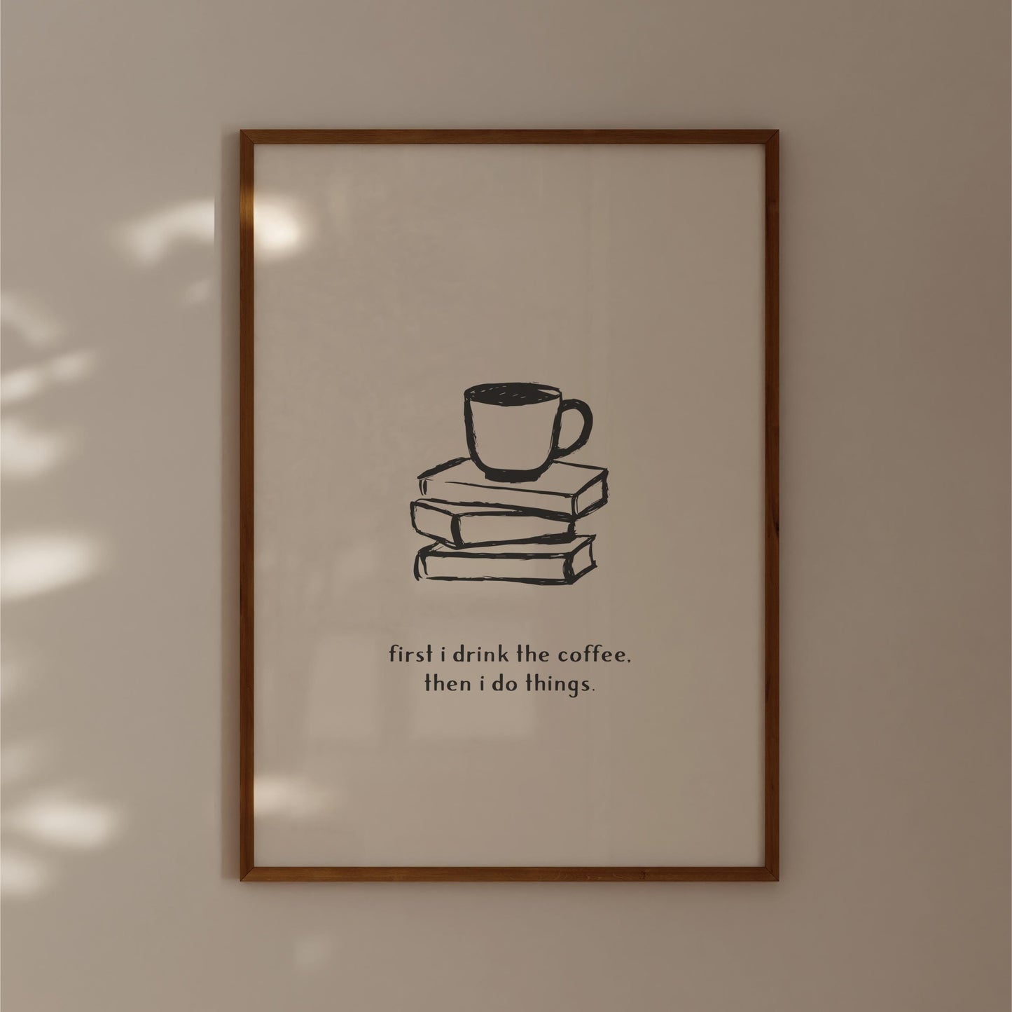A framed poster with a simple black and white illustration of a cup of coffee on top of three books, accompanied by the text "first I drink the coffee. then I do things."