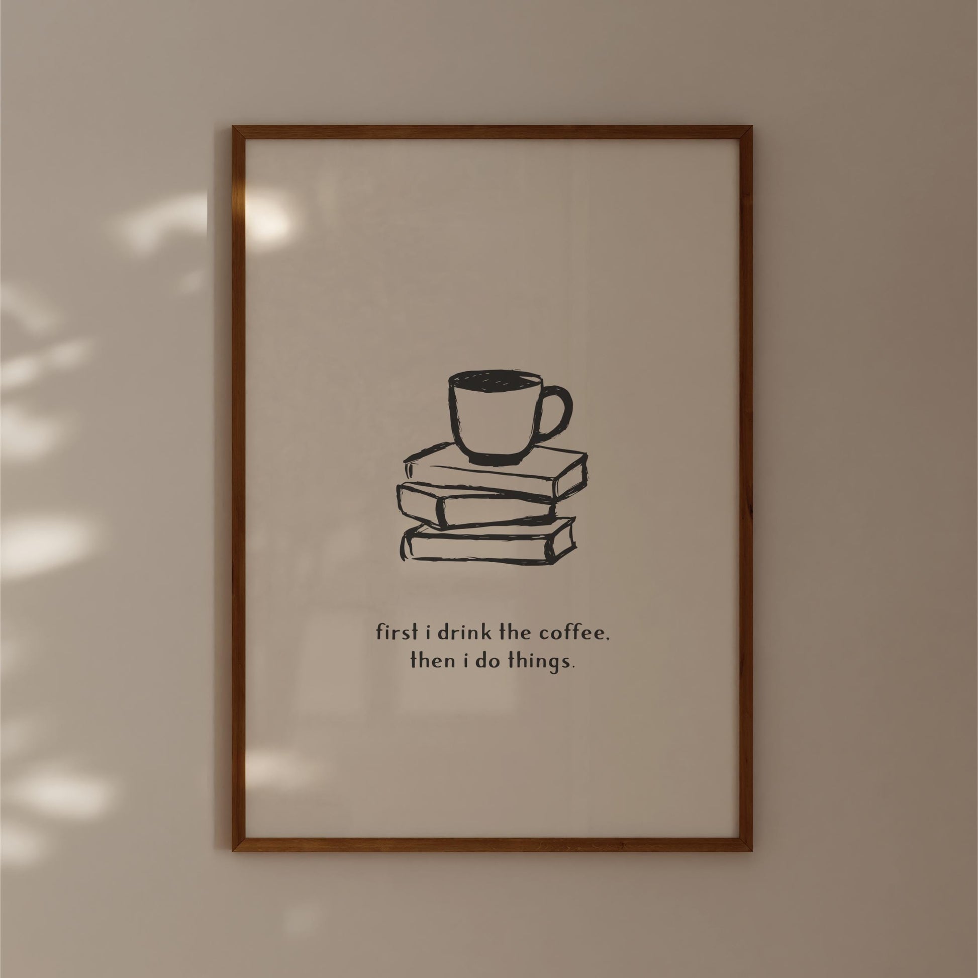 A framed poster with a simple black and white illustration of a cup of coffee on top of three books, accompanied by the text "first I drink the coffee. then I do things."