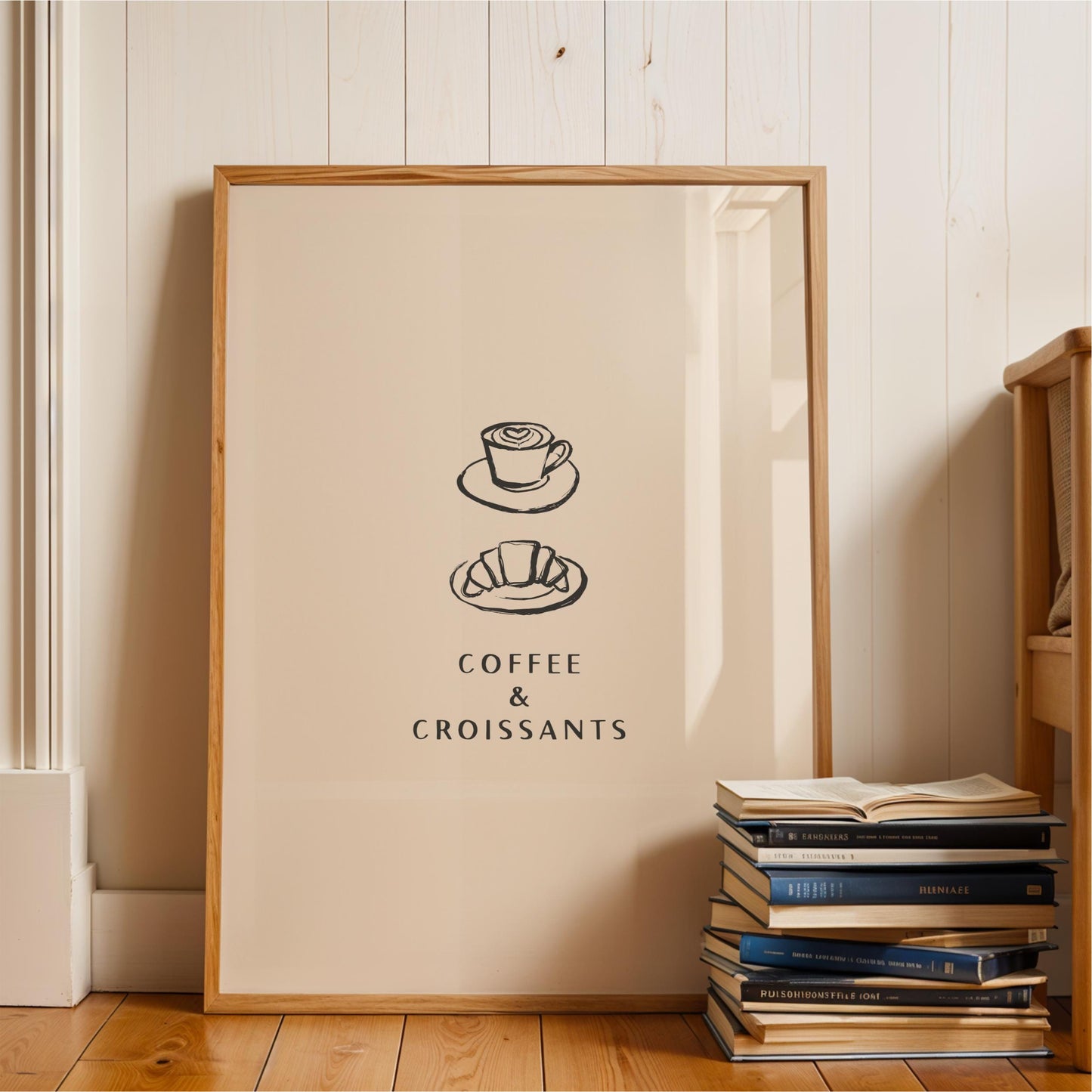 A framed poster with the text "COFFEE & CROISSANTS" is displayed on a wall next to a stack of books.