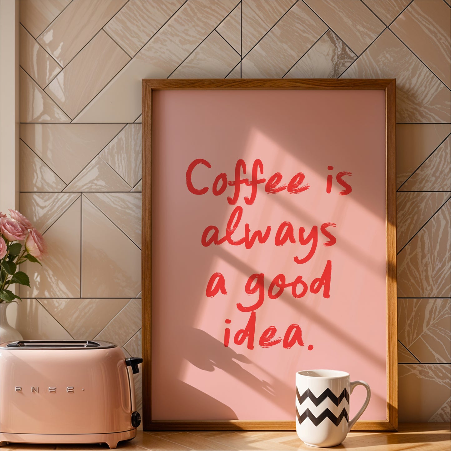 a pink poster with the text "Coffee is always a good idea" in red lettering, placed on a kitchen counter next to a pink toaster and a white coffee mug.