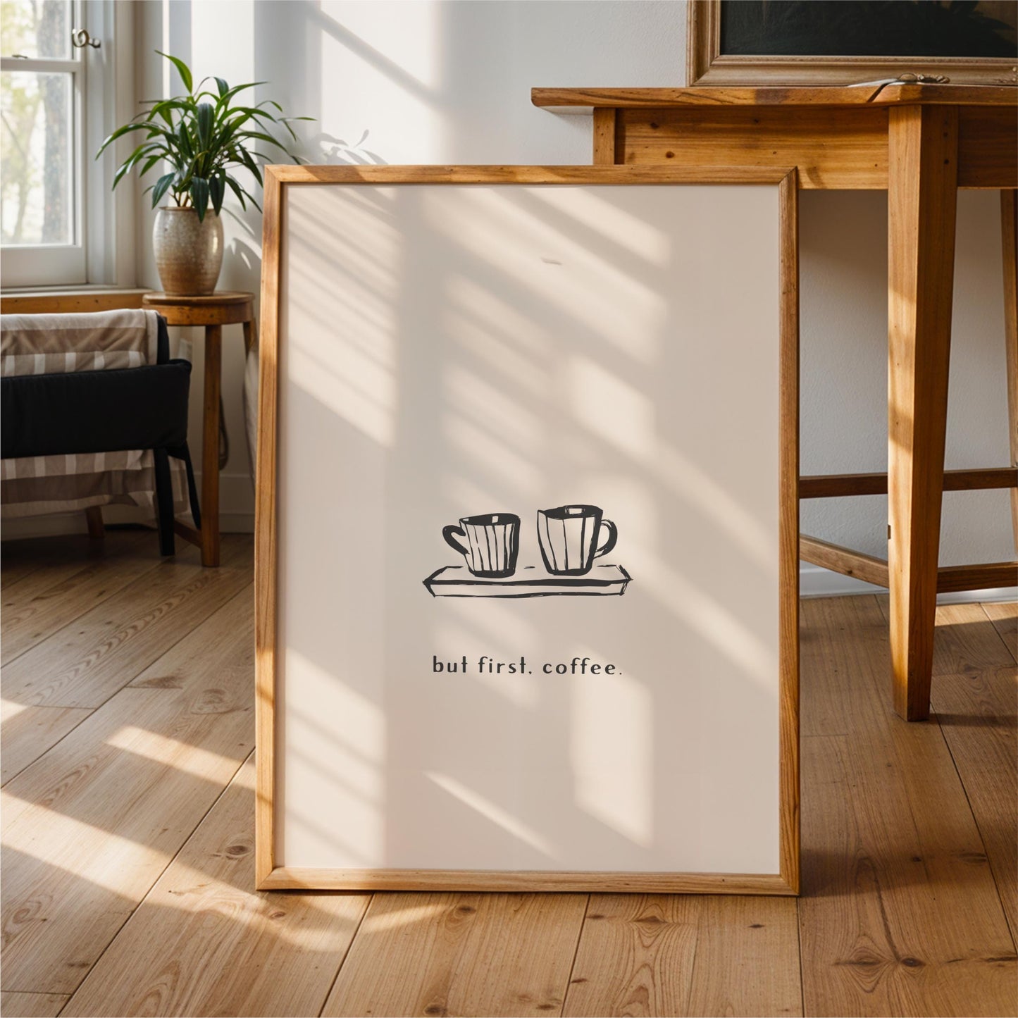 A framed poster with a simple black and white illustration of two coffee cups on a tray, accompanied by the text "but first coffee" in a casual, handwritten style.