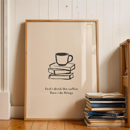 A framed poster with a simple black and white illustration of a coffee cup on a stack of books, accompanied by the text "first I drink the coffee. then I do things."