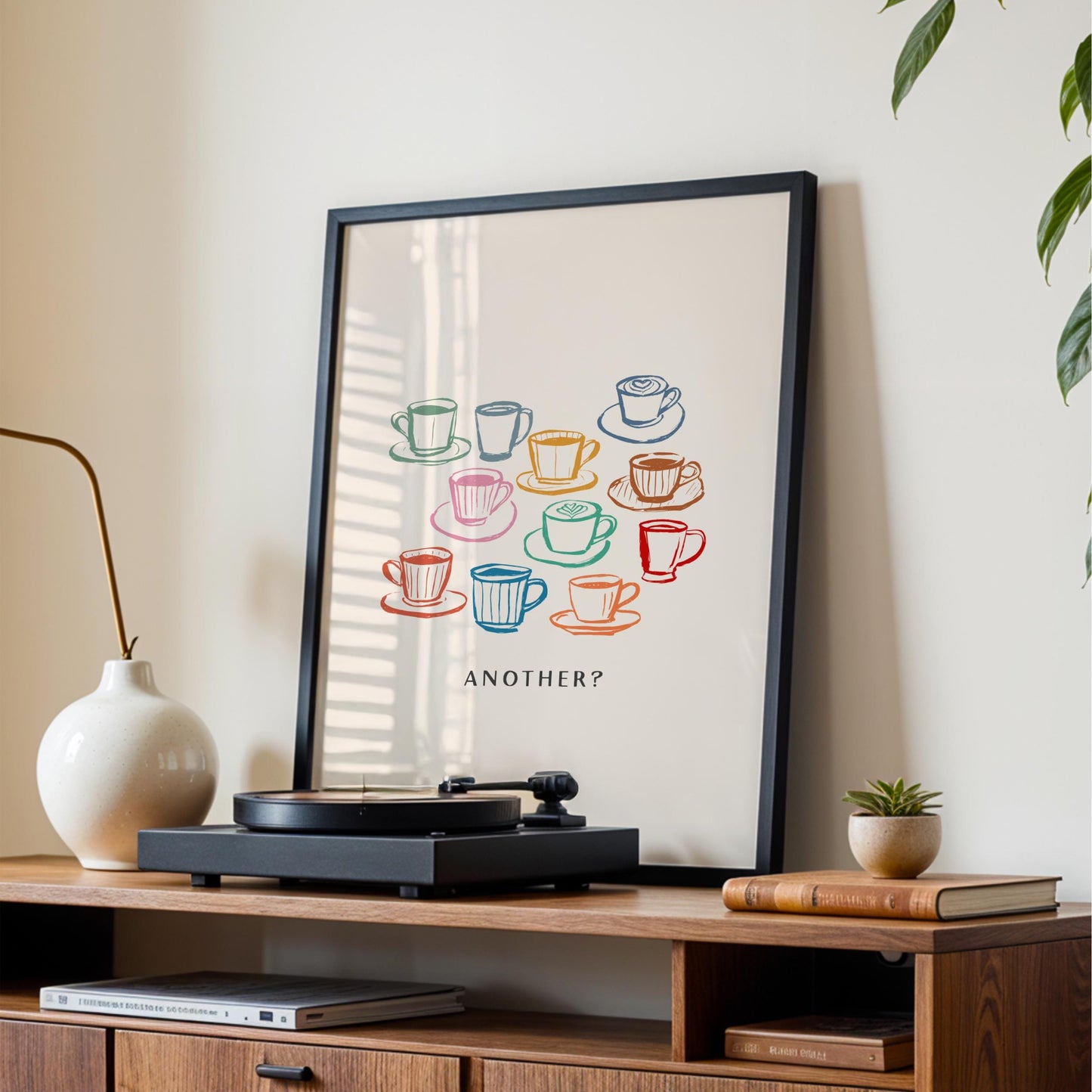 a framed poster with a colorful illustration of various coffee cups and saucers, along with the text "Another?" displayed on it. The poster is placed on a wooden entertainment center, which also holds a record player and some books.