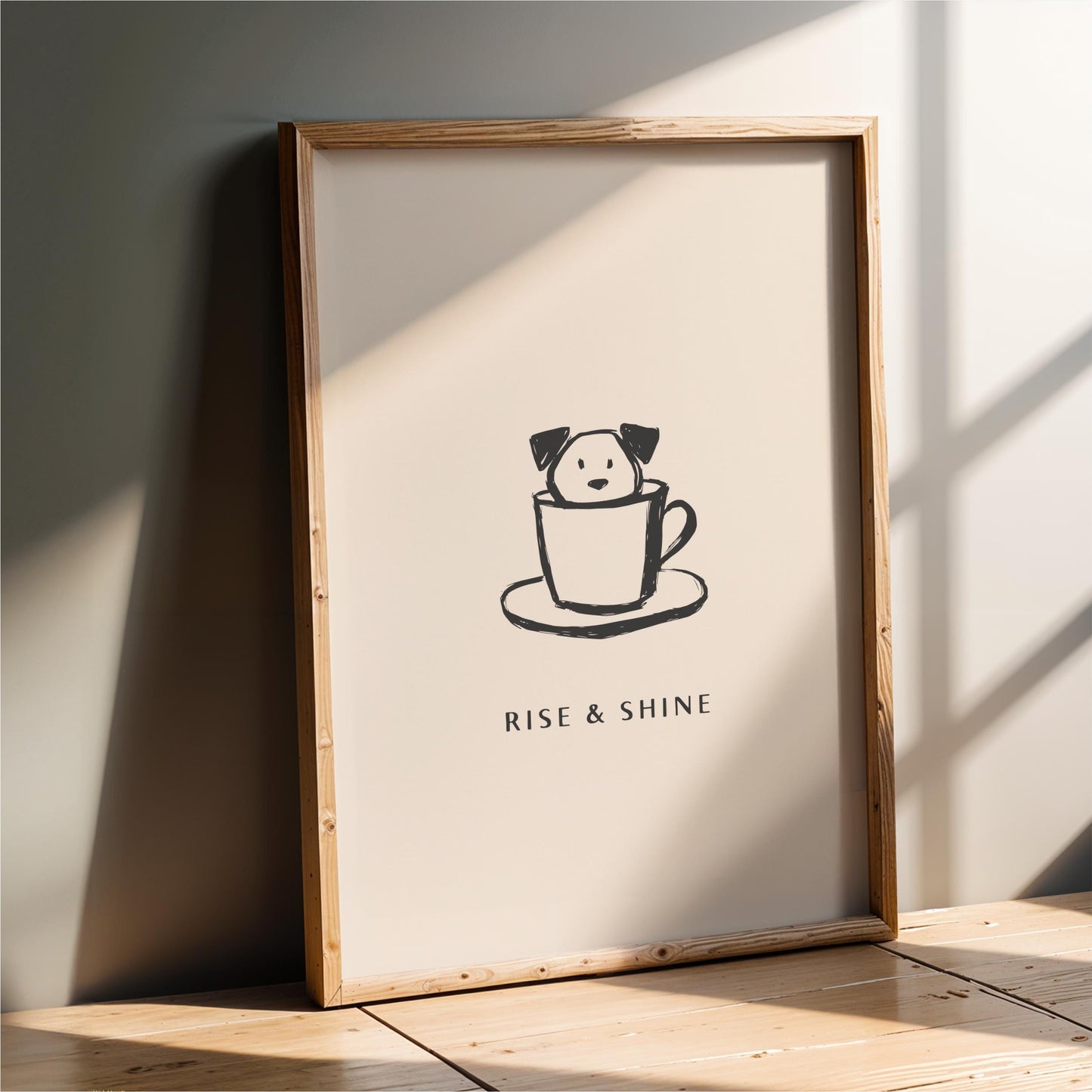 A framed poster with a simple black and white illustration of a dog in a cup, accompanied by the text "RISE & SHINE" in a smaller font.
