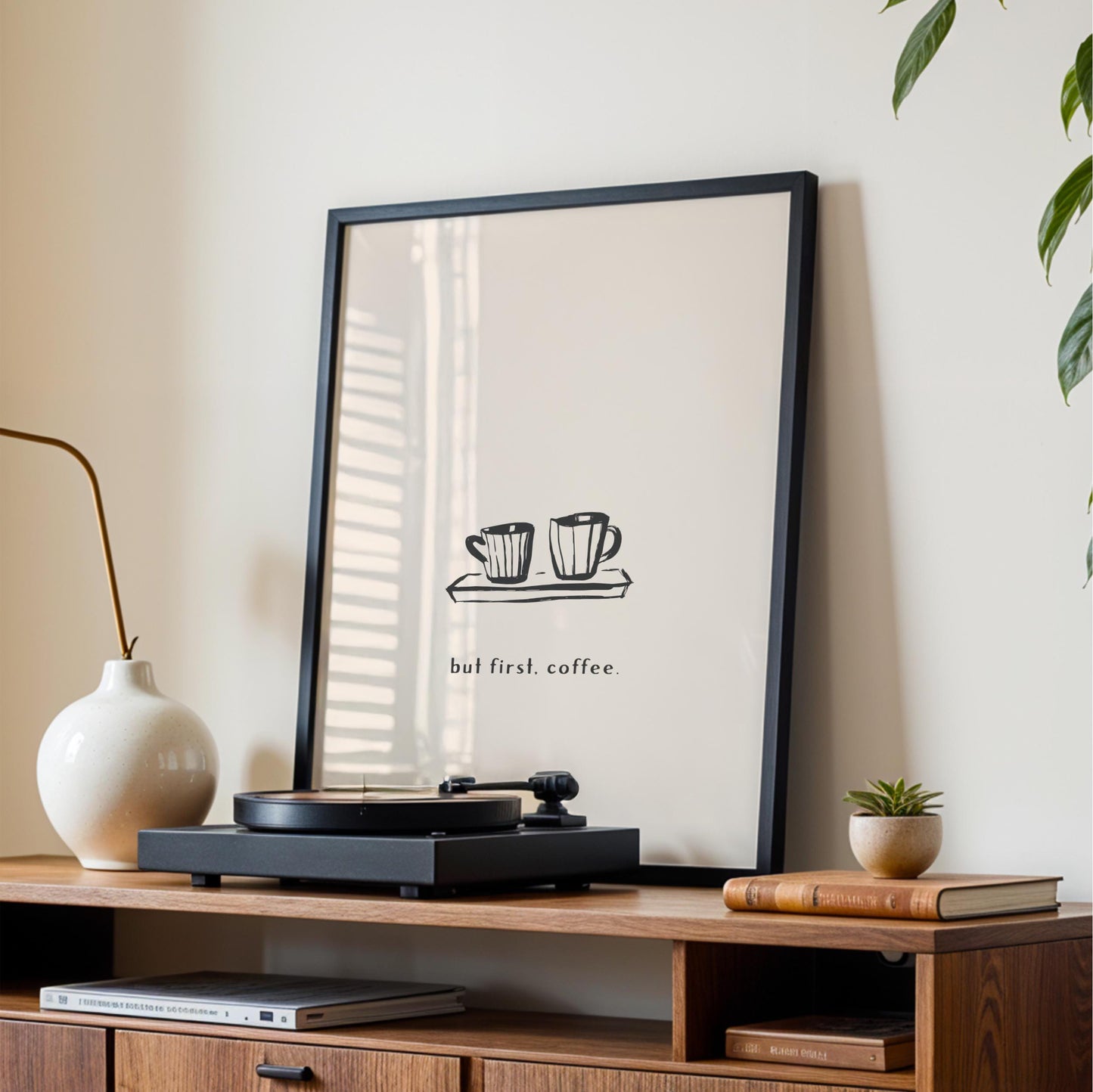 a framed poster with a coffee cup illustration and the text "but first, coffee." The poster is displayed on a wall above a wooden entertainment center with a record player and other items.