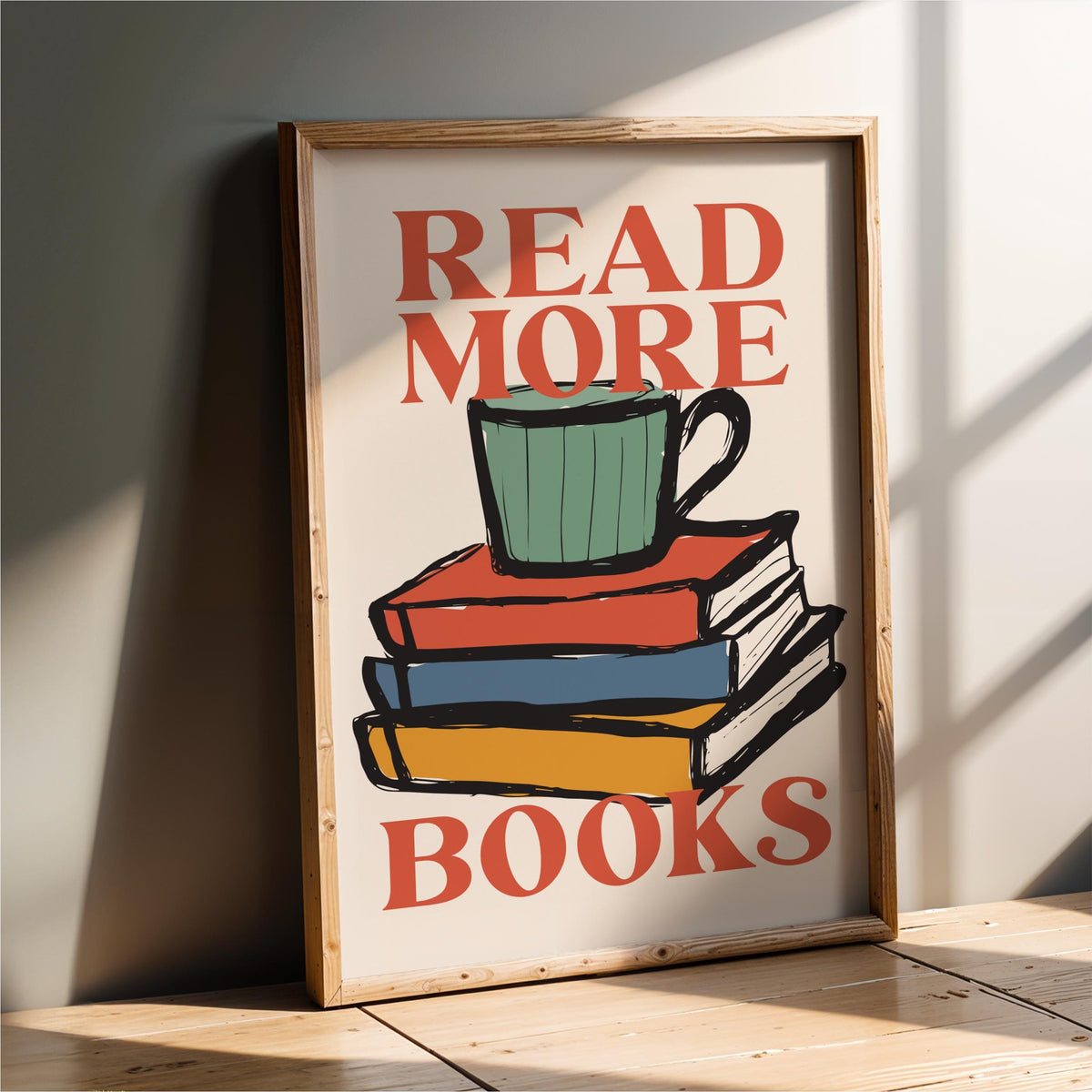 A framed poster with the text "READ MORE BOOKS" and an illustration of a stack of colorful books with a green mug on top.