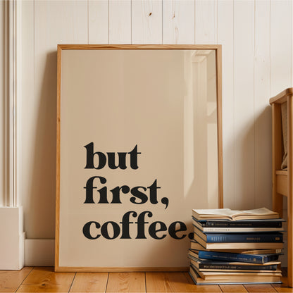 A framed poster with the text "but first, coffee" is leaning against a wall, with a stack of books next to it.