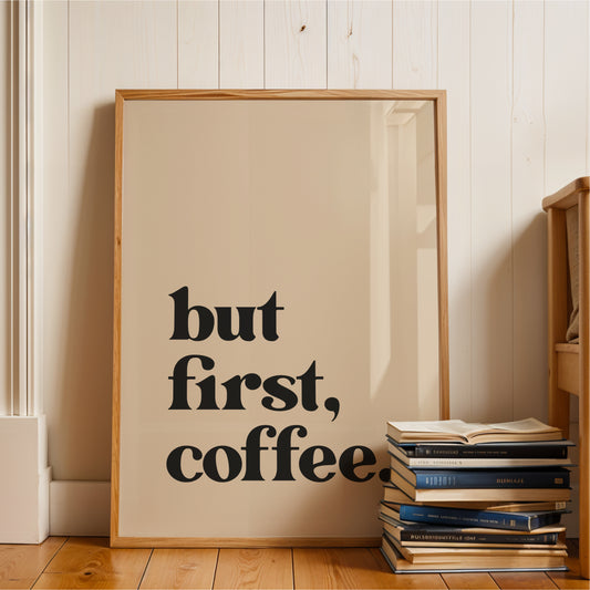 A framed poster with the text "but first, coffee" is leaning against a wall, with a stack of books next to it.