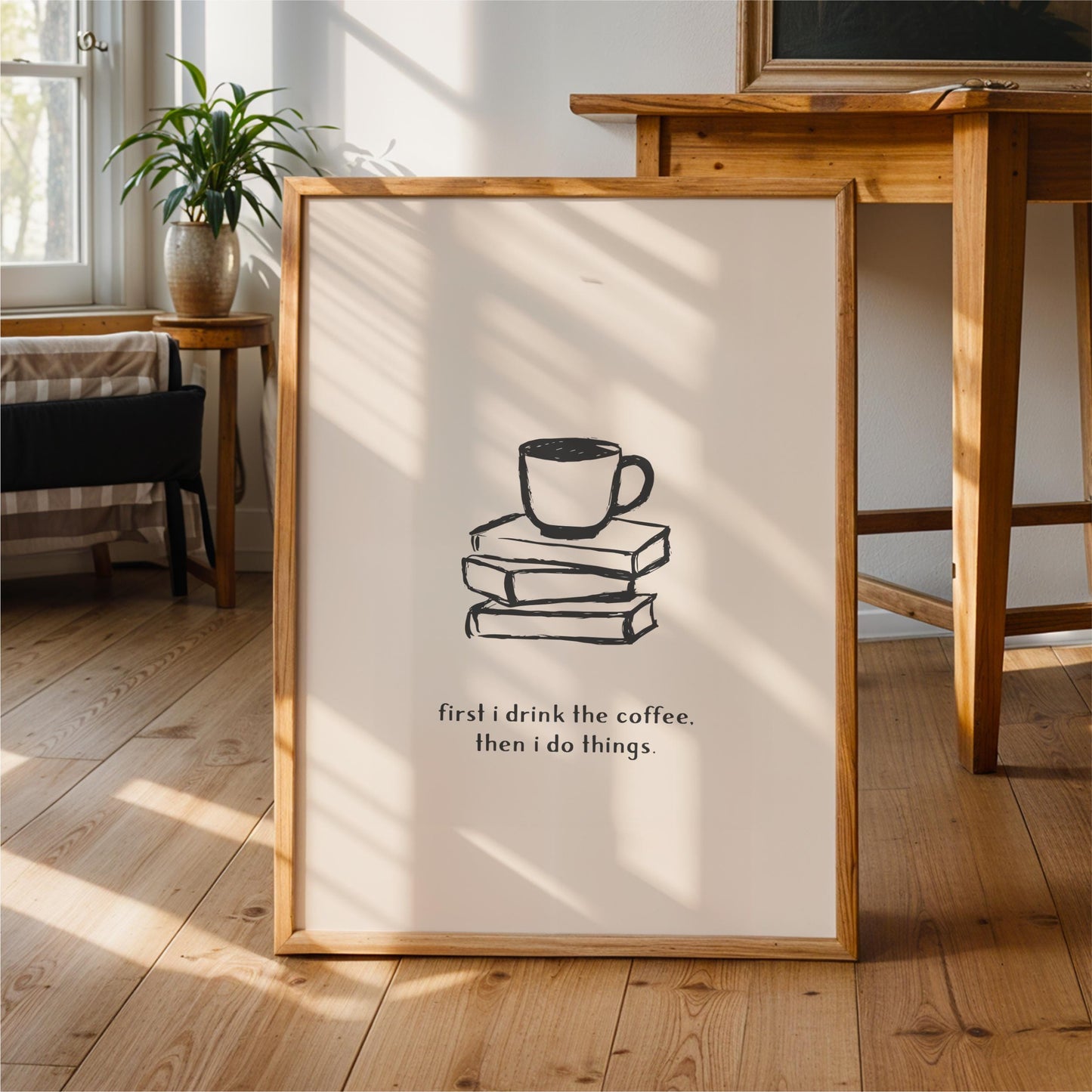 A framed poster with a simple black and white illustration of a coffee cup on a stack of books, accompanied by the text "first I drink the coffee. Then I do things."