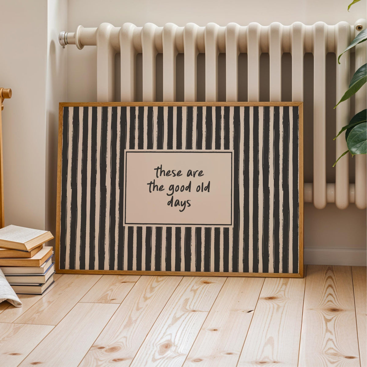 A framed poster with a black and white striped pattern and the text "These are the good old days" is displayed on a wooden floor next to a white radiator.