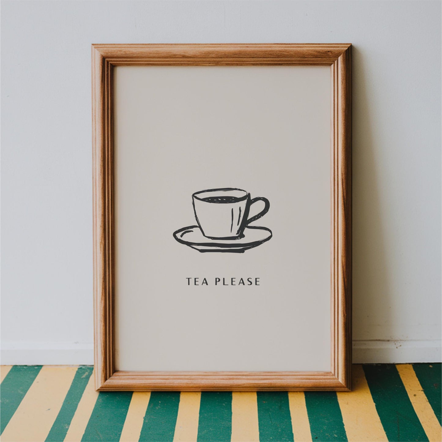 A framed print with a simple black and white illustration of a cup of tea on a saucer, accompanied by the text "TEA PLEASE" in a bold, capitalized font.