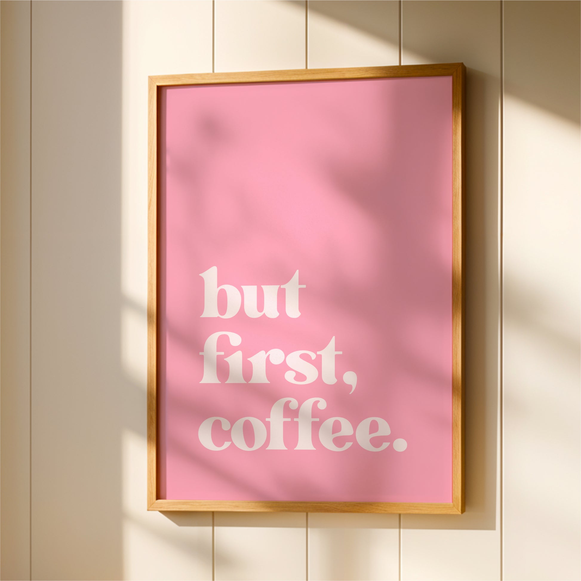A framed poster with the text "but first, coffee" in white letters against a pink background.