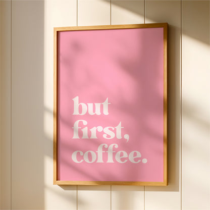 A framed poster with the text "but first, coffee" in white letters against a pink background.