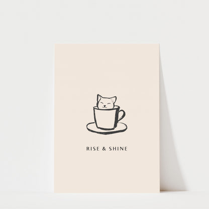 A simple black and white illustration of a cat sitting inside a coffee cup, accompanied by the text "RISE & SHINE" below the image.